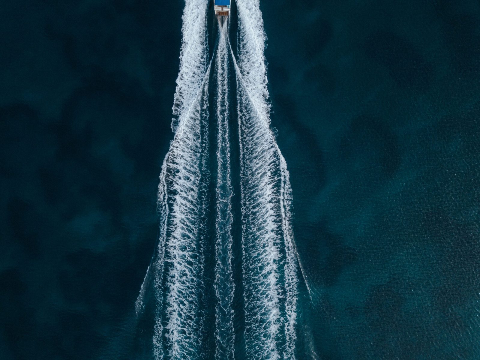 An aerial overhead shot of a motorboat sailing forward in the middle of the ocean